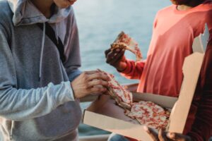crop unrecognizable men eating pizza on waterfront